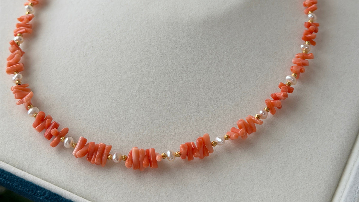 A coral and pearl beaded necklace with small gold spacer beads and a gold clasp, displayed on a white jewelry box.